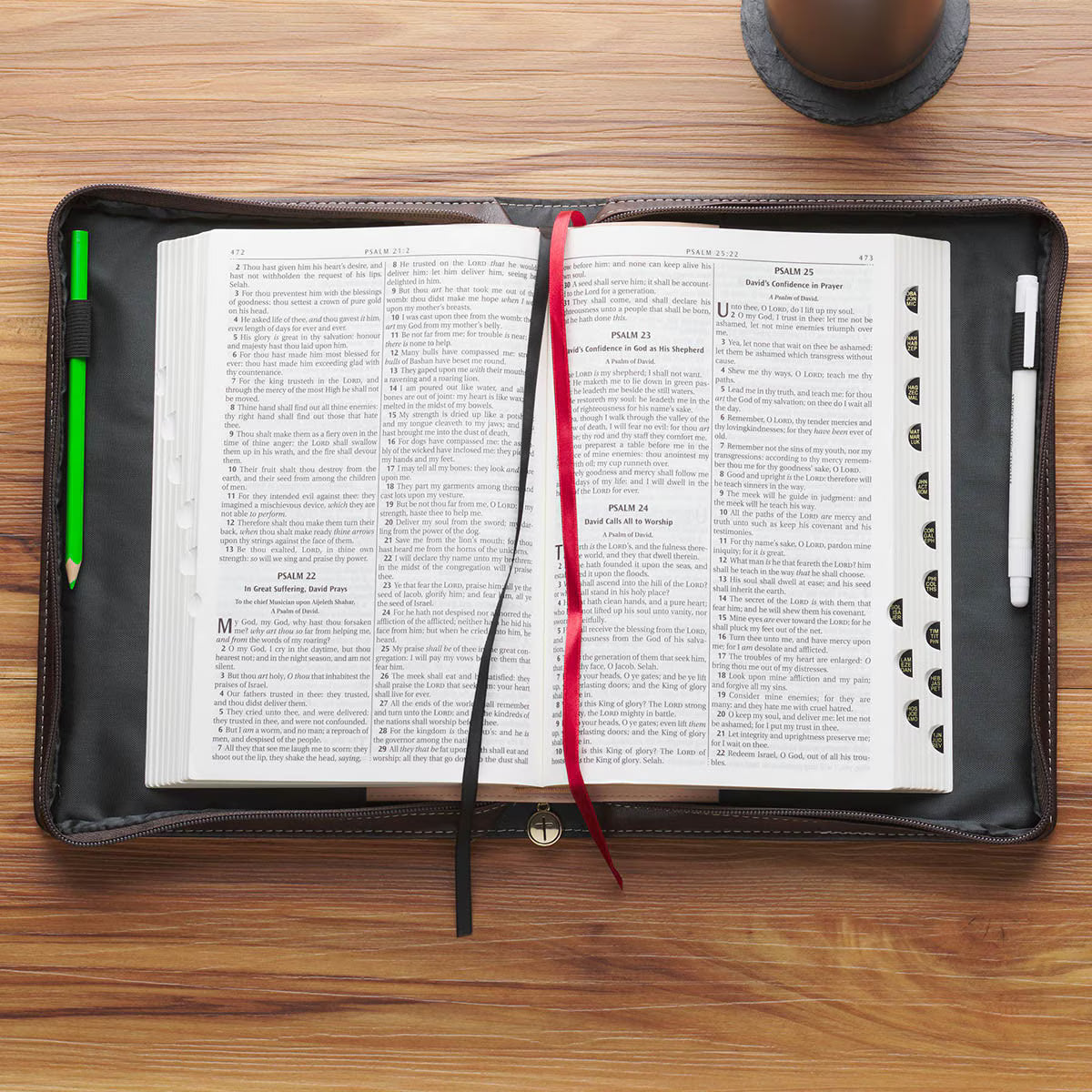 Open Bible inside dark brown leather cover with pen slots, red and black ribbon bookmarks on wooden table