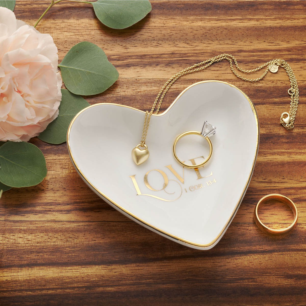 Heart-shaped white ceramic trinket tray with gold rim and 1 Corinthians 13:4 love script, holding rings and necklace