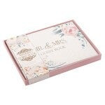Medium wedding guest book with peachy-pink floral faux leather cover and 1 John 4:19 inscription on front