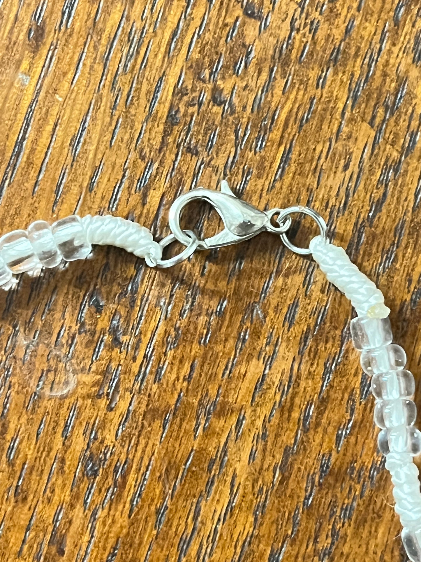 Close-up of white and clear bead rosary lobster clasp on wooden surface, part of White Rosary in a Glass Bottle gift set