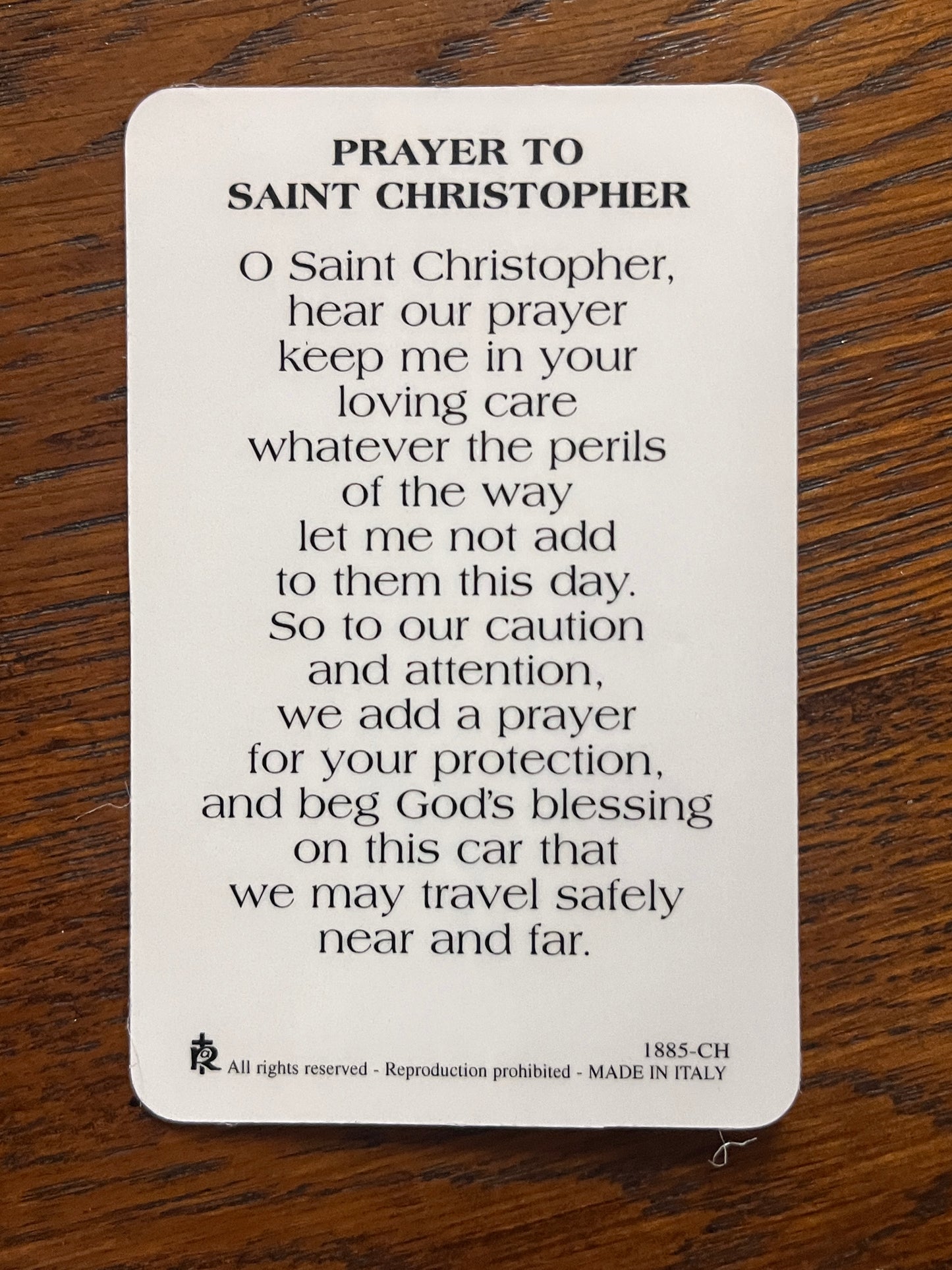 Prayer card with printed St. Christopher prayer for travel safety on white background with wood surface beneath