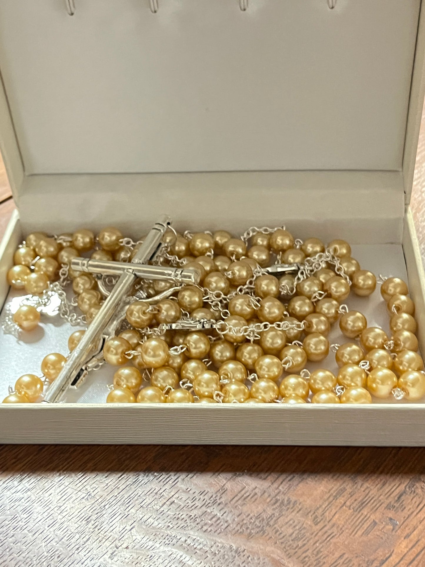 10mm gold faux pearl rosary with silver cross chain resting inside an open white box on wooden surface