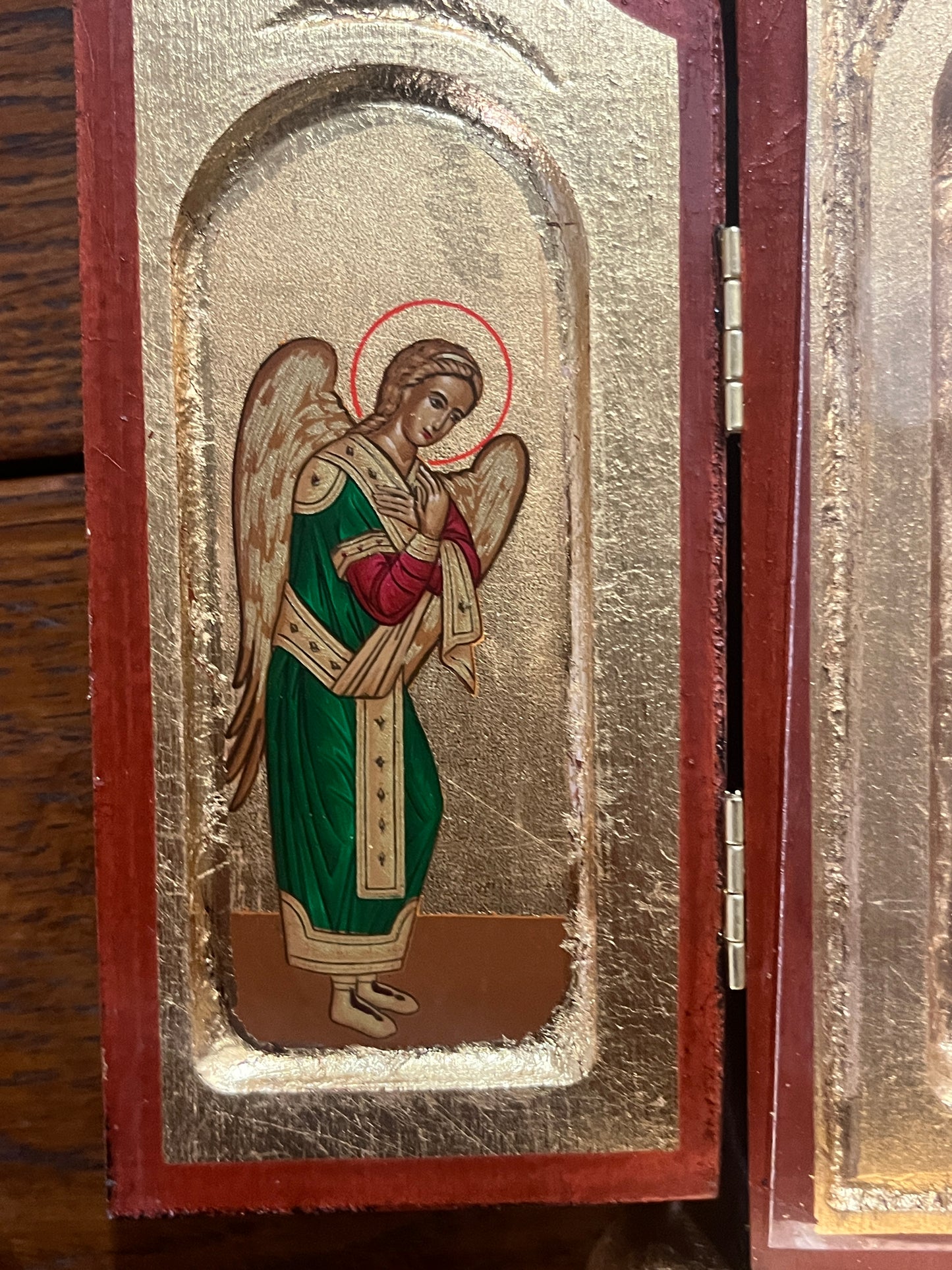 Close-up of painted angel in green and red robes with gold halo on gilded background of wooden Greek icon triptych panel