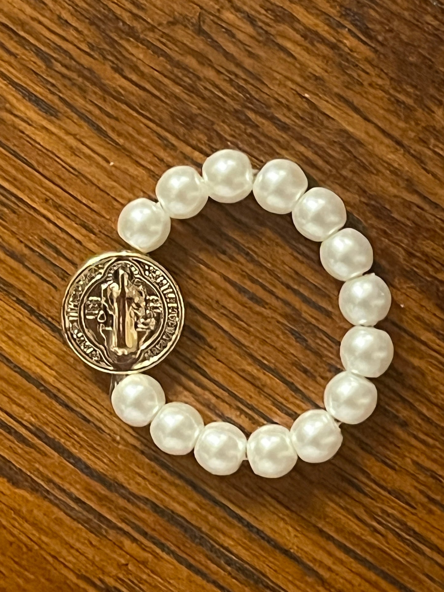 White stretch ring with pearl-like beads and gold Benedict medal resting on wooden surface