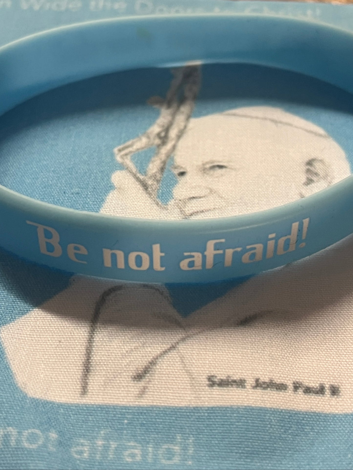 Blue rubber bracelet with "Be not afraid!" text over black and white image of Saint John Paul II relic handkerchief