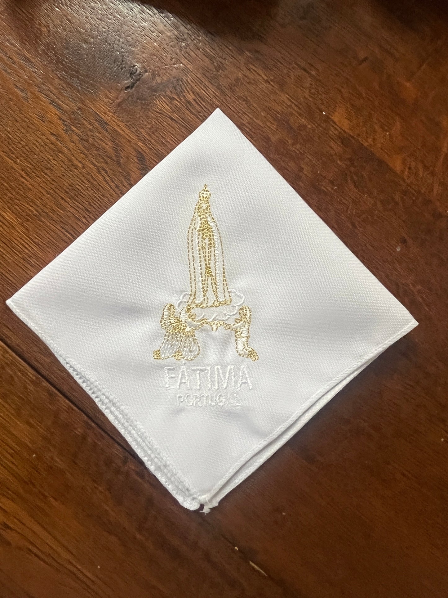 White handkerchief embroidered with gold and white Our Lady of Fatima and Portugal text on wooden background