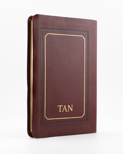 Brown leather-bound book titled TAN with gold embossed border and text on plain white background