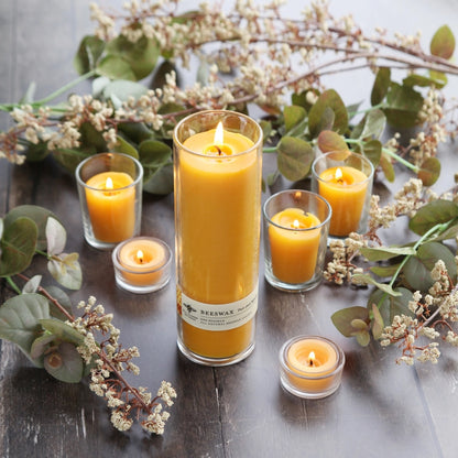 Tall Sanctuary glass beeswax candle surrounded by smaller lit beeswax candles and dried greenery on wood table