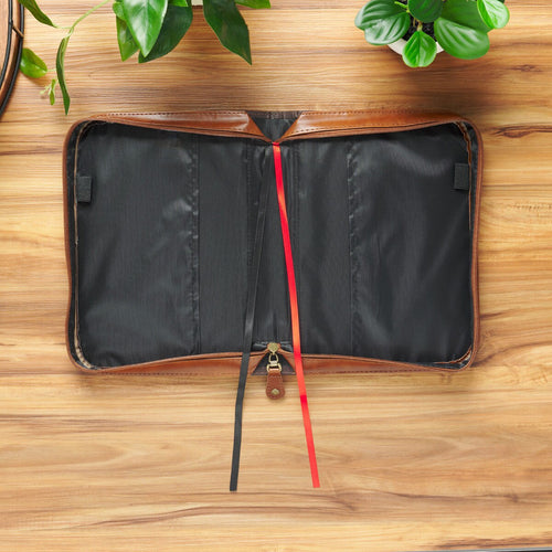 Open honey-brown and espresso faux leather Bible cover with black and red bookmarks on wooden surface