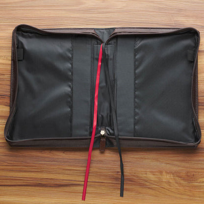 Open brown faux leather Bible cover with black interior lining and red and black ribbon page markers on wooden surface