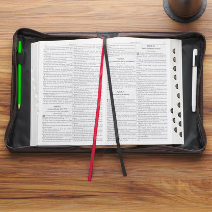 Open brown faux leather Bible cover with black and red ribbon markers on wooden surface with pen and stylus holder