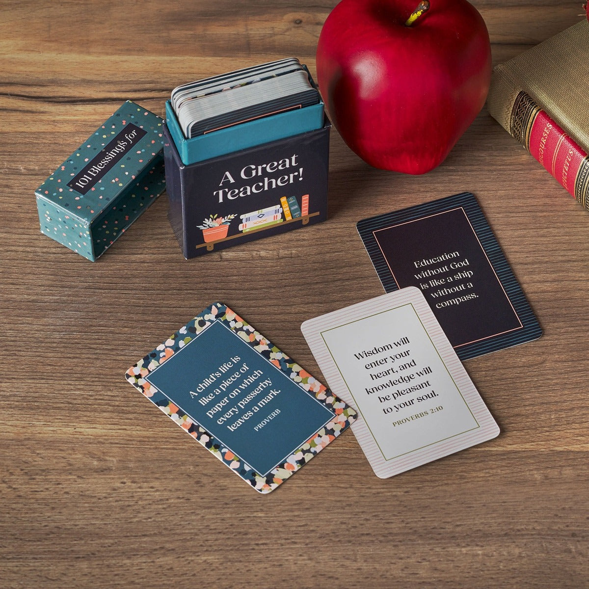 101 Blessings A Great Teacher teal confetti box with inspiring blessing cards and decorative book and apple on wood surface