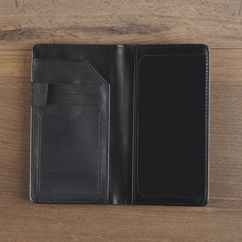 Open black faux leather checkbook wallet with card slots and pen holder on wooden surface