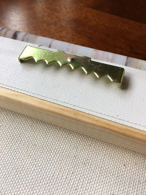 Gold sawtooth canvas hanger attached to the back of a wooden stretcher frame for hanging wall art