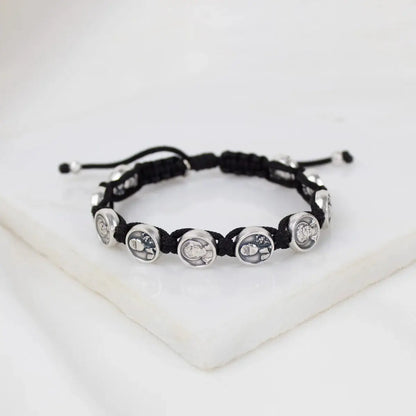 Black cord bracelet with silver Carlo Acutis medals intricately linked, displayed on white marble surface