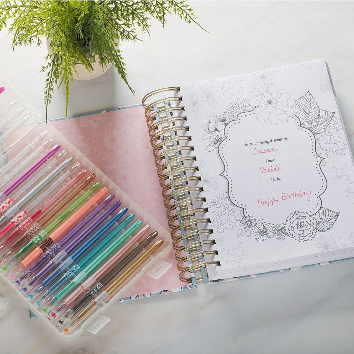 Wirebound women’s devotional coloring book open to personalized message with floral designs and colorful gel pens set