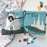 Fabric quiet book titled "Wrapped in Mary’s Mantle" with soft sewn figures and interactive flaps for children’s religious learning