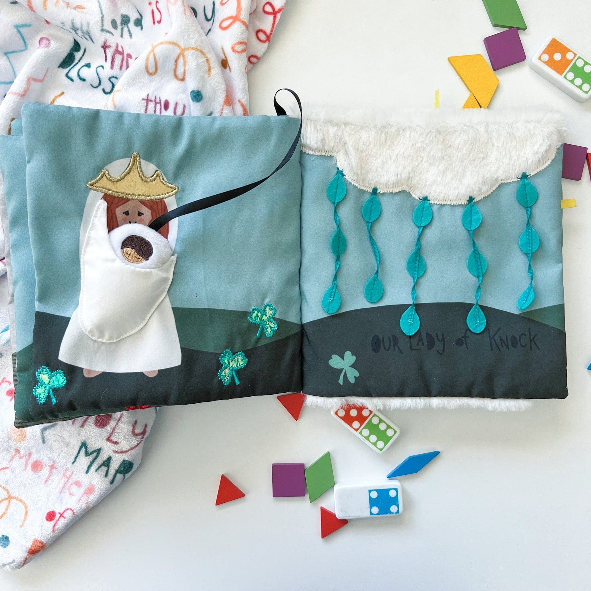 Soft fabric Mass quiet book open to Mary holding infant Jesus and Our Lady of Knock with blue and green details