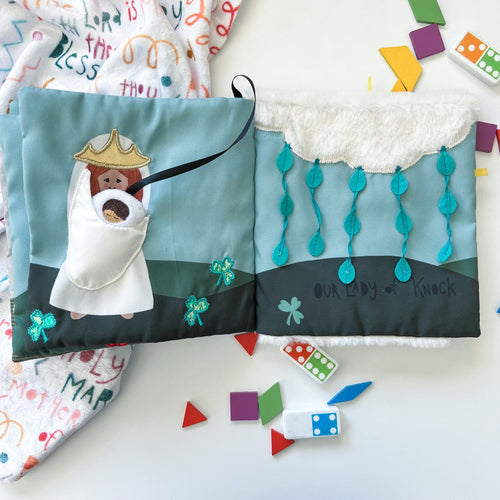 Soft fabric Mass quiet book open to Mary holding infant Jesus and Our Lady of Knock with blue and green details