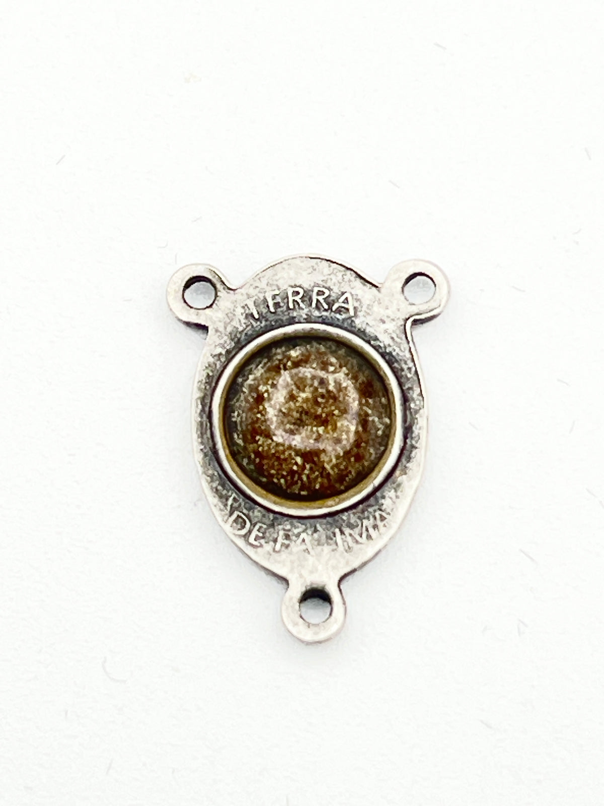 A small silver-toned metal jewelry finding or charm with three prongs and a round textured brown center, photographed on a plain white background.