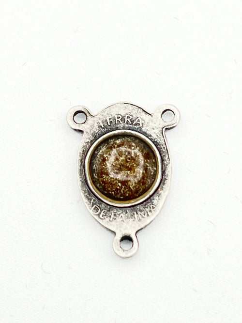 A small silver-toned metal jewelry finding or charm with three prongs and a round textured brown center, photographed on a plain white background.