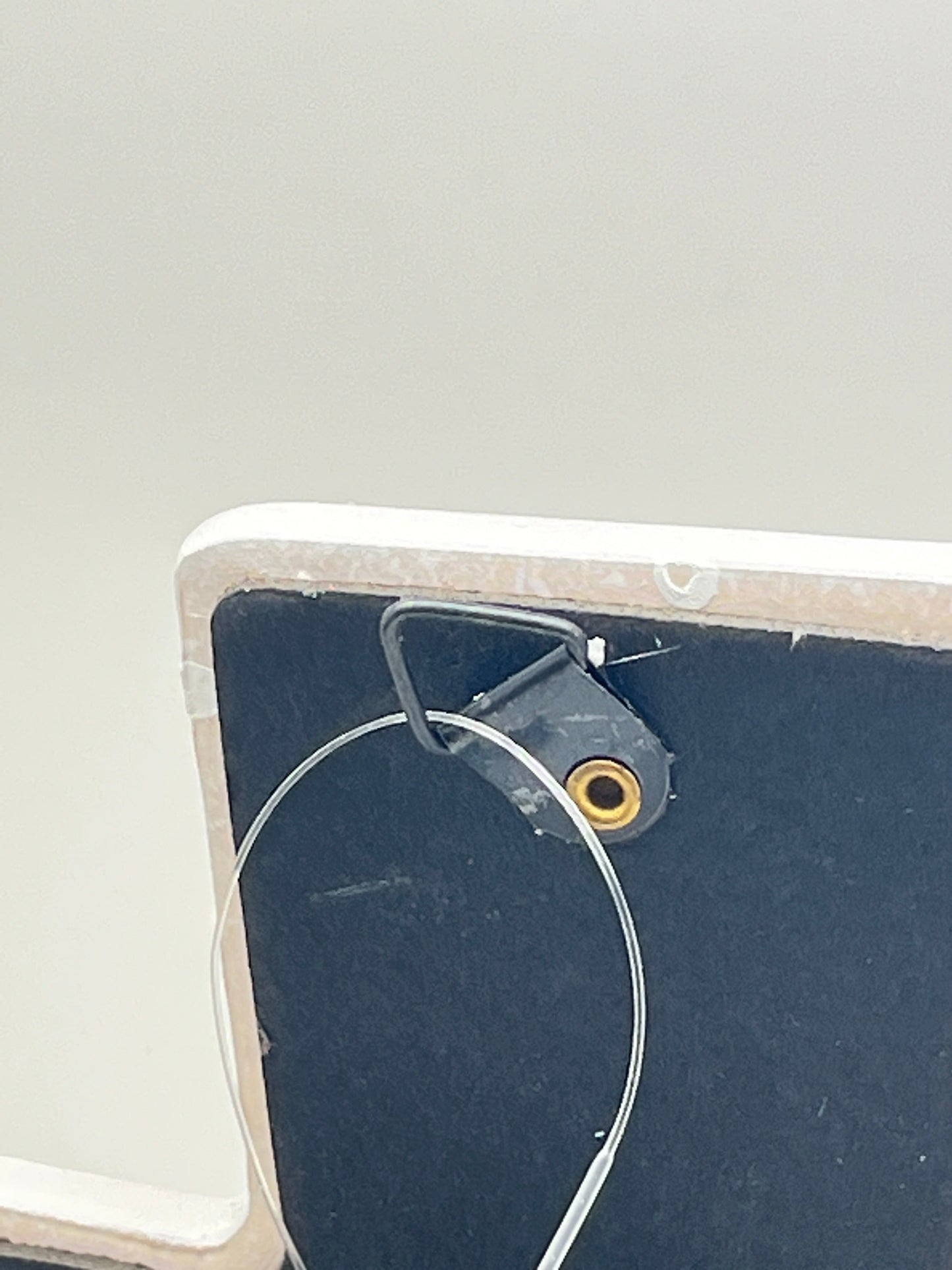 Back view of Love Never Fails ceramic wall cross with black easel stand and wire hanger, 7.75 inches tall.