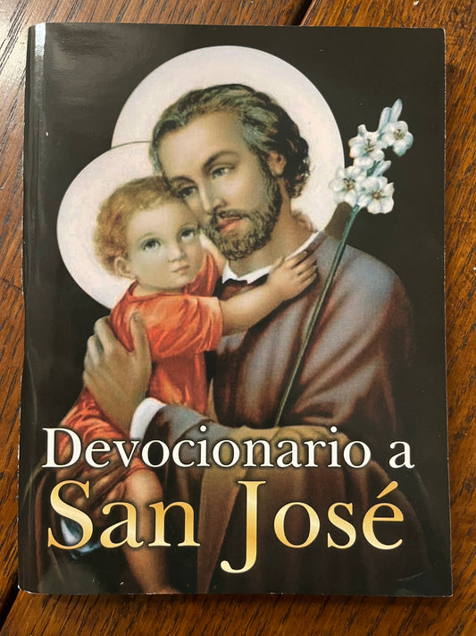Devotional book cover titled Devocionario a San José featuring Saint Joseph holding baby Jesus with lilies on a dark background