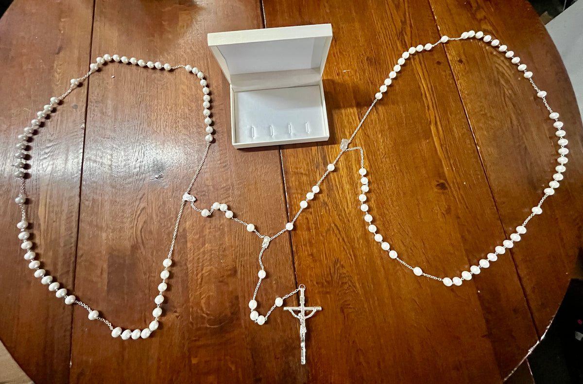 White 12MM faux pearl wedding lasso rosary with silver-tone crucifix and Madonna and child centerpiece displayed on wood table