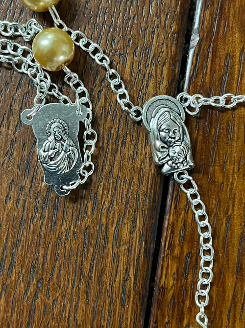 Close-up of silver rosary connector showing Virgin Mary and baby Jesus medallions on wood background