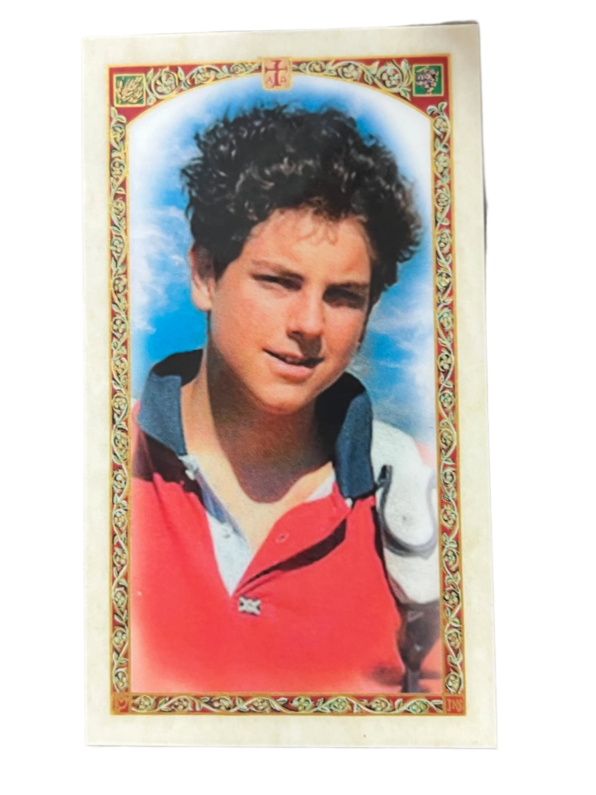 Laminated holy card featuring portrait of St. Carlo Acutis with decorative gold border and blue sky background
