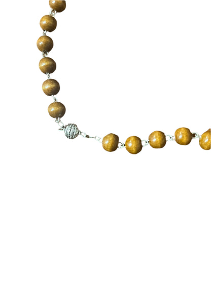 Close-up of Fatima brown wood rosary beads with silver textured Our Father bead on white background