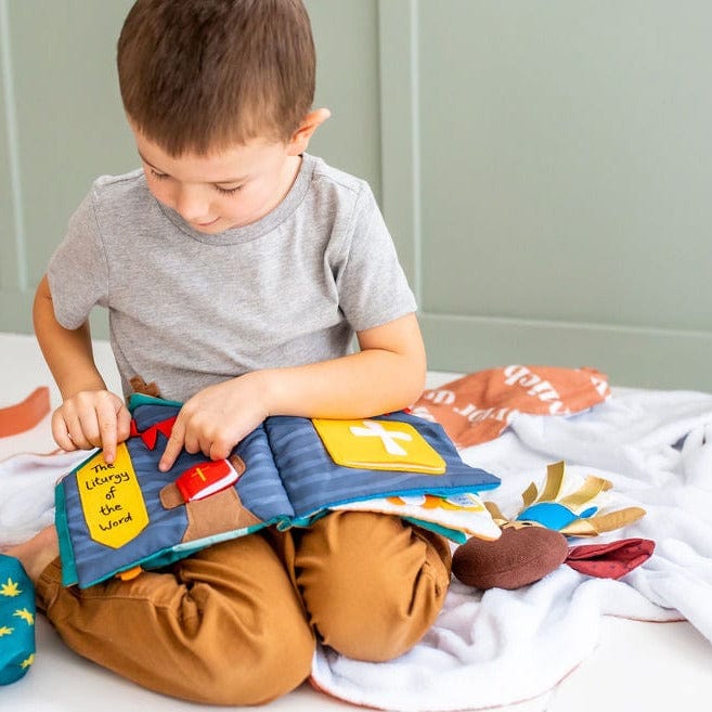Young boy sitting on floor engaging with interactive pages of Catholic Mass Quiet Book for children