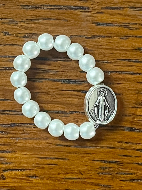Stretch ring with white beads and silver Miraculous Medal centerpiece on wooden background