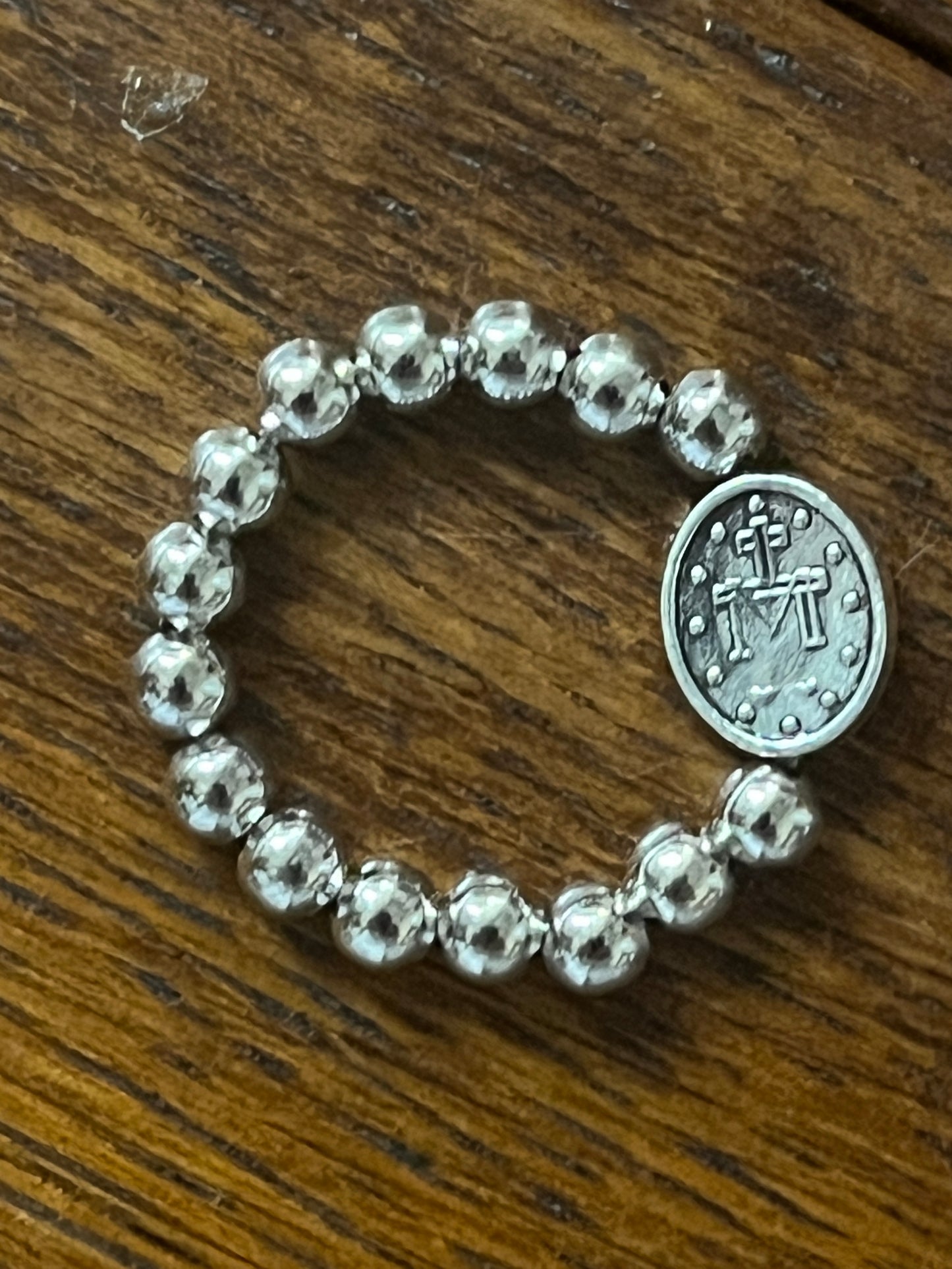 Silver stretch ring with polished round beads and oval Miraculous Medal charm on wooden surface