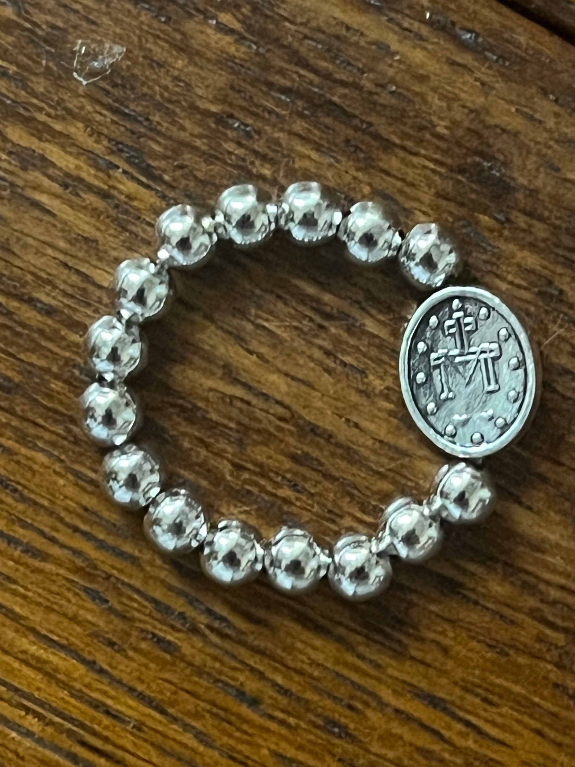 Silver stretch ring with polished round beads and oval Miraculous Medal charm on wooden surface