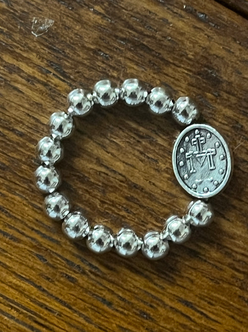 Silver stretch ring with polished round beads and oval Miraculous Medal charm on wooden surface