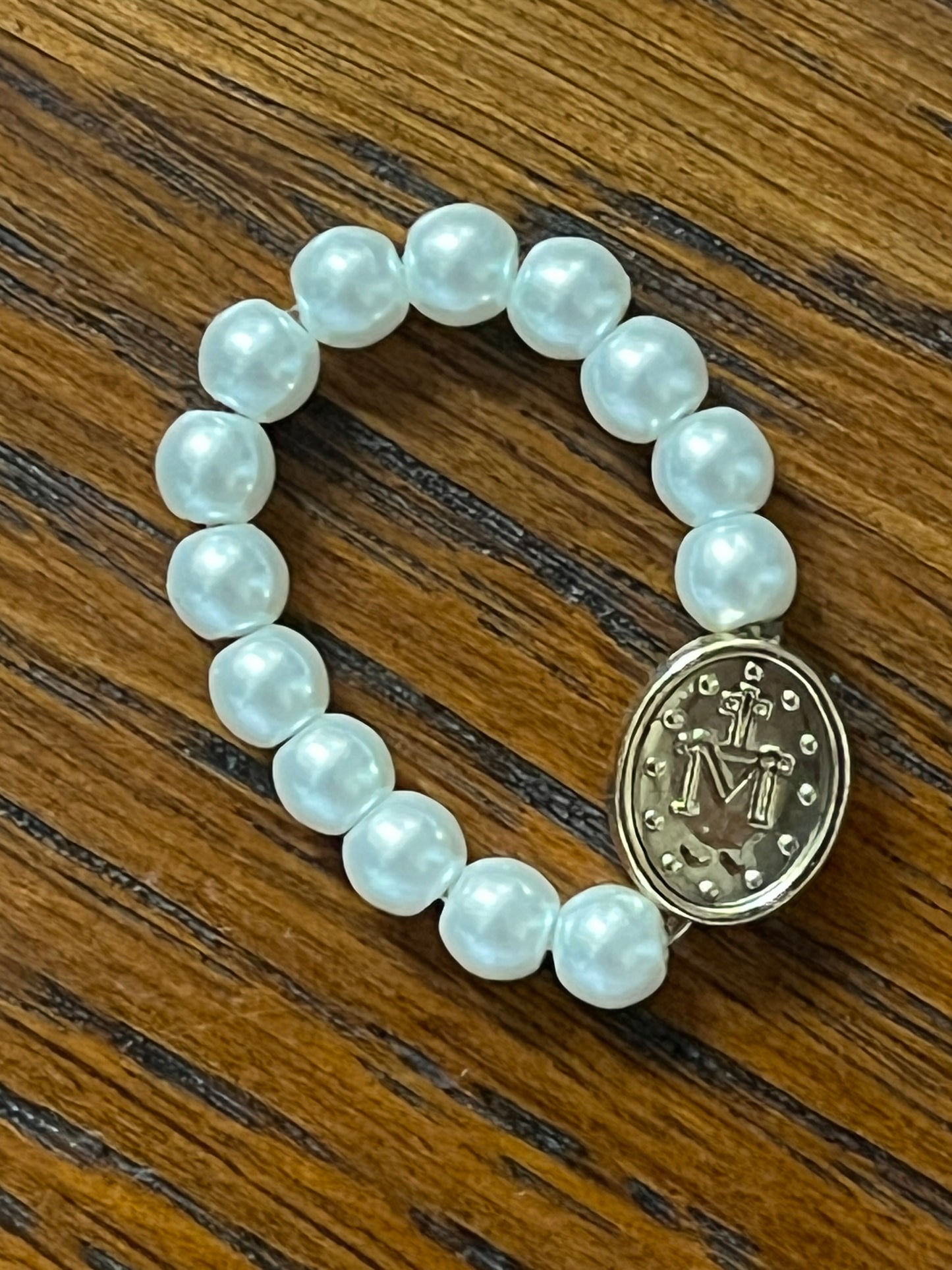 Stretch ring with white pearl-like beads and gold Miraculous Medal charm on wooden surface background