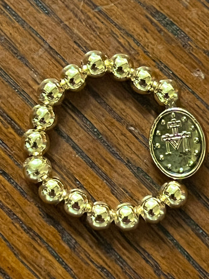 Gold-tone Miraculous Medal stretch ring with polished round beads on wooden surface background