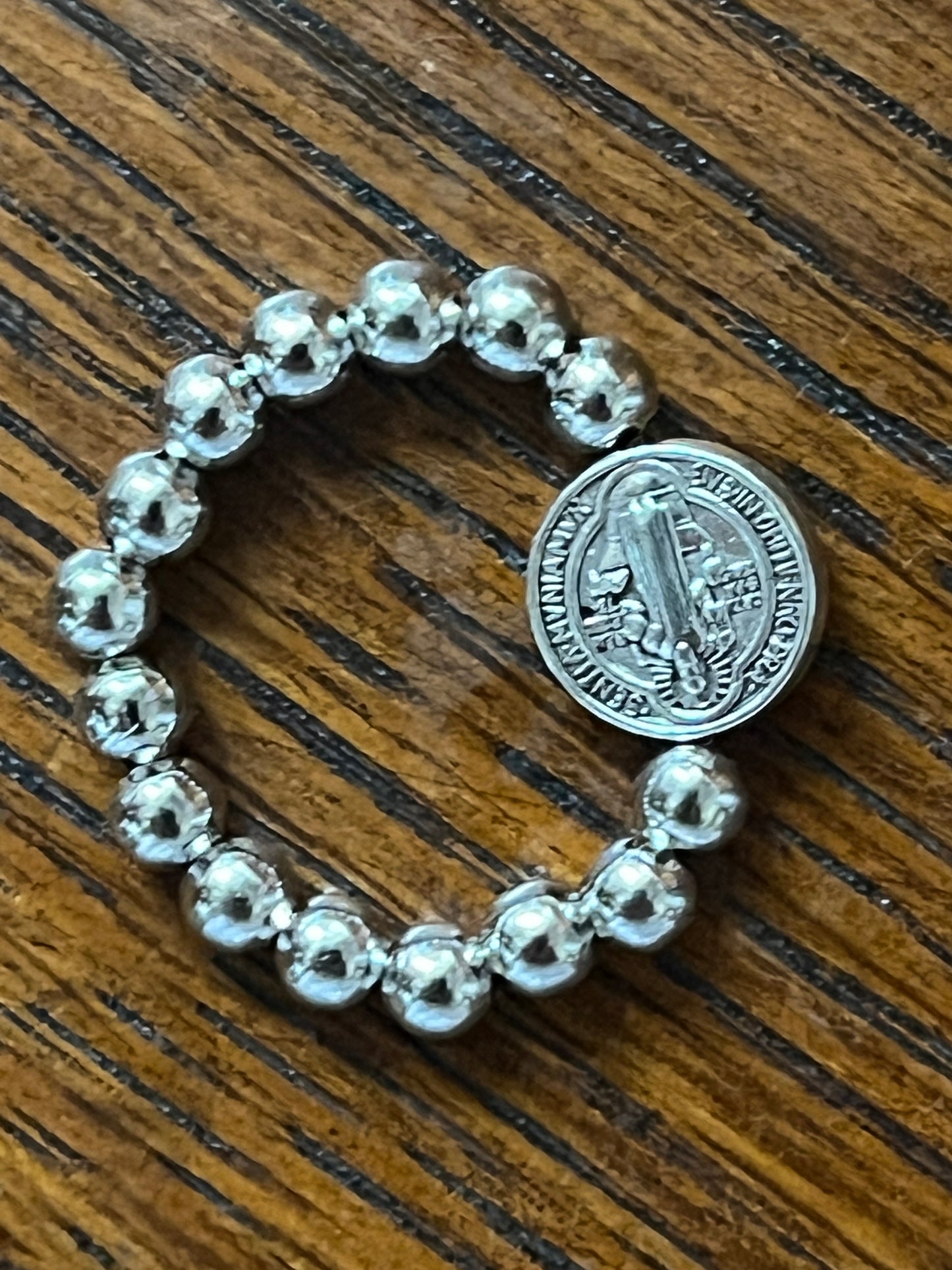 Silver stretch ring with polished round beads and detailed Benedict medal centerpiece on wooden surface