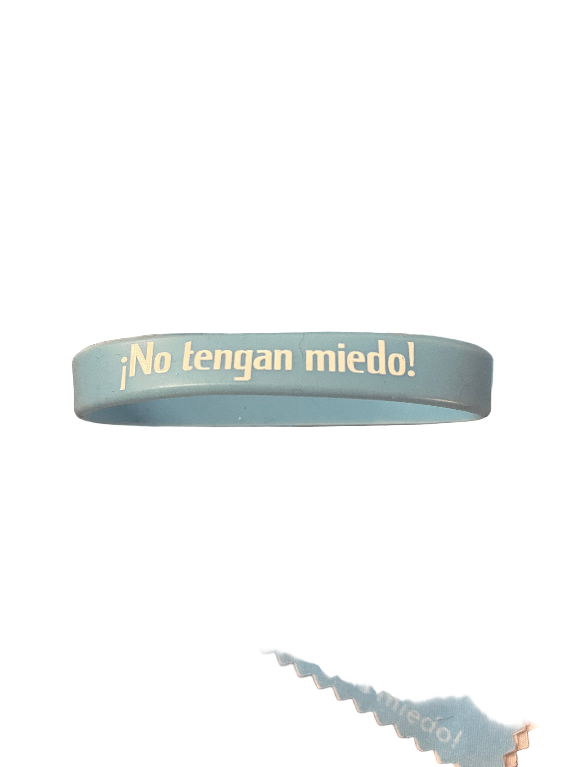 Light blue rubber bracelet with "No tengan miedo!" text in white on one side against white background
