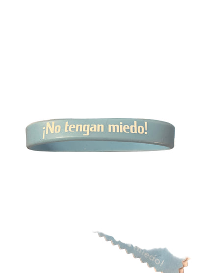 Light blue rubber bracelet with "No tengan miedo!" text in white on one side against white background
