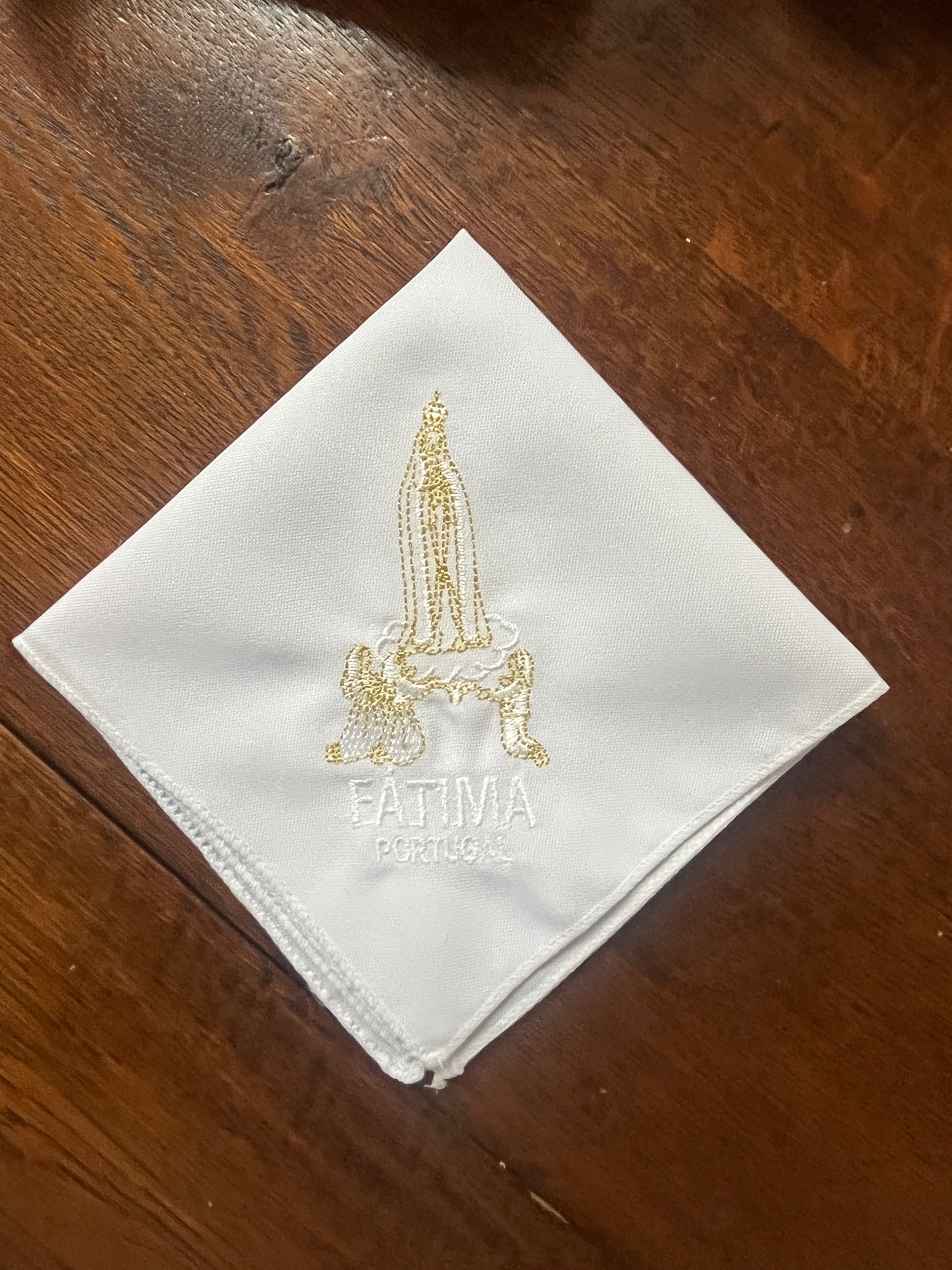 White handkerchief embroidered with gold and white Our Lady of Fatima and Portugal text on wooden background