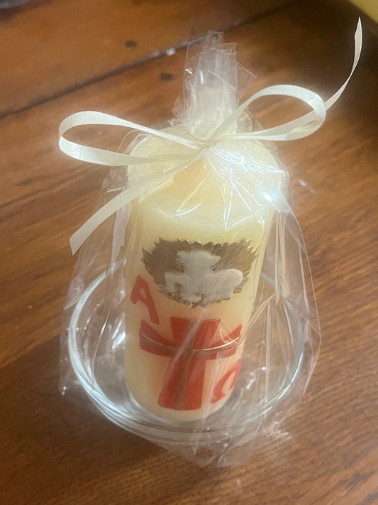 Beeswax Paschal candle decorated with red cross and silver dove wrapped in clear plastic, placed on clear glass plate