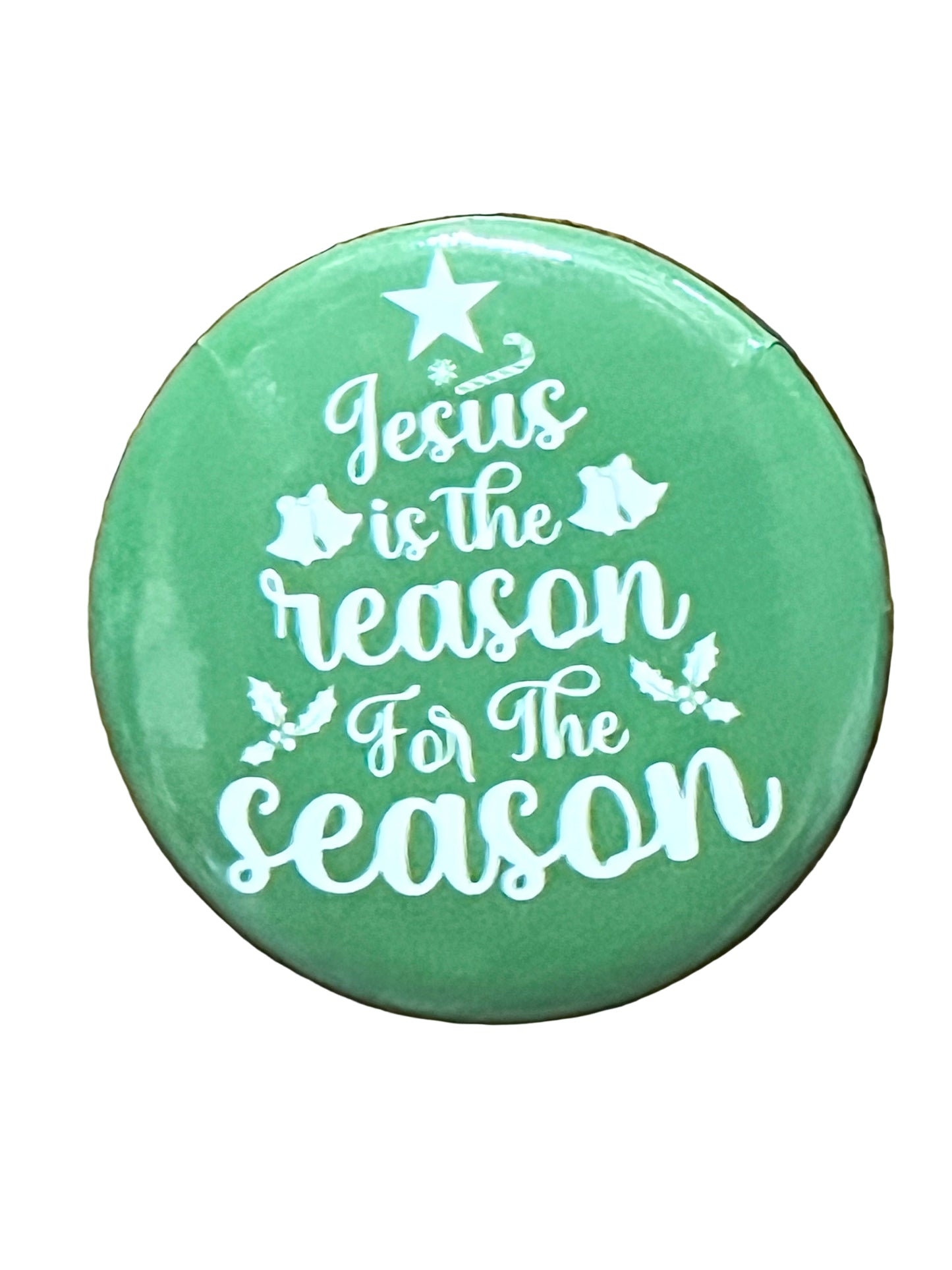 Green Christmas button with white text "Jesus is the reason for the season" decorated with star, bells, and holly leaves