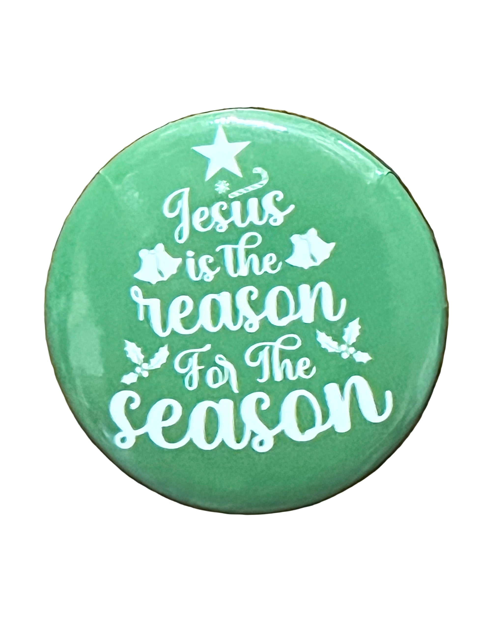 Green Christmas button with white text "Jesus is the reason for the season" decorated with star, bells, and holly leaves
