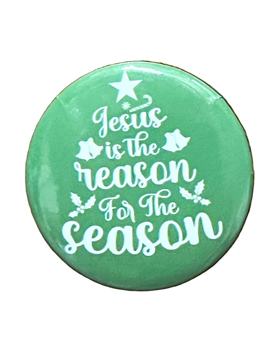 Green Christmas button with white text "Jesus is the reason for the season" decorated with star, bells, and holly leaves