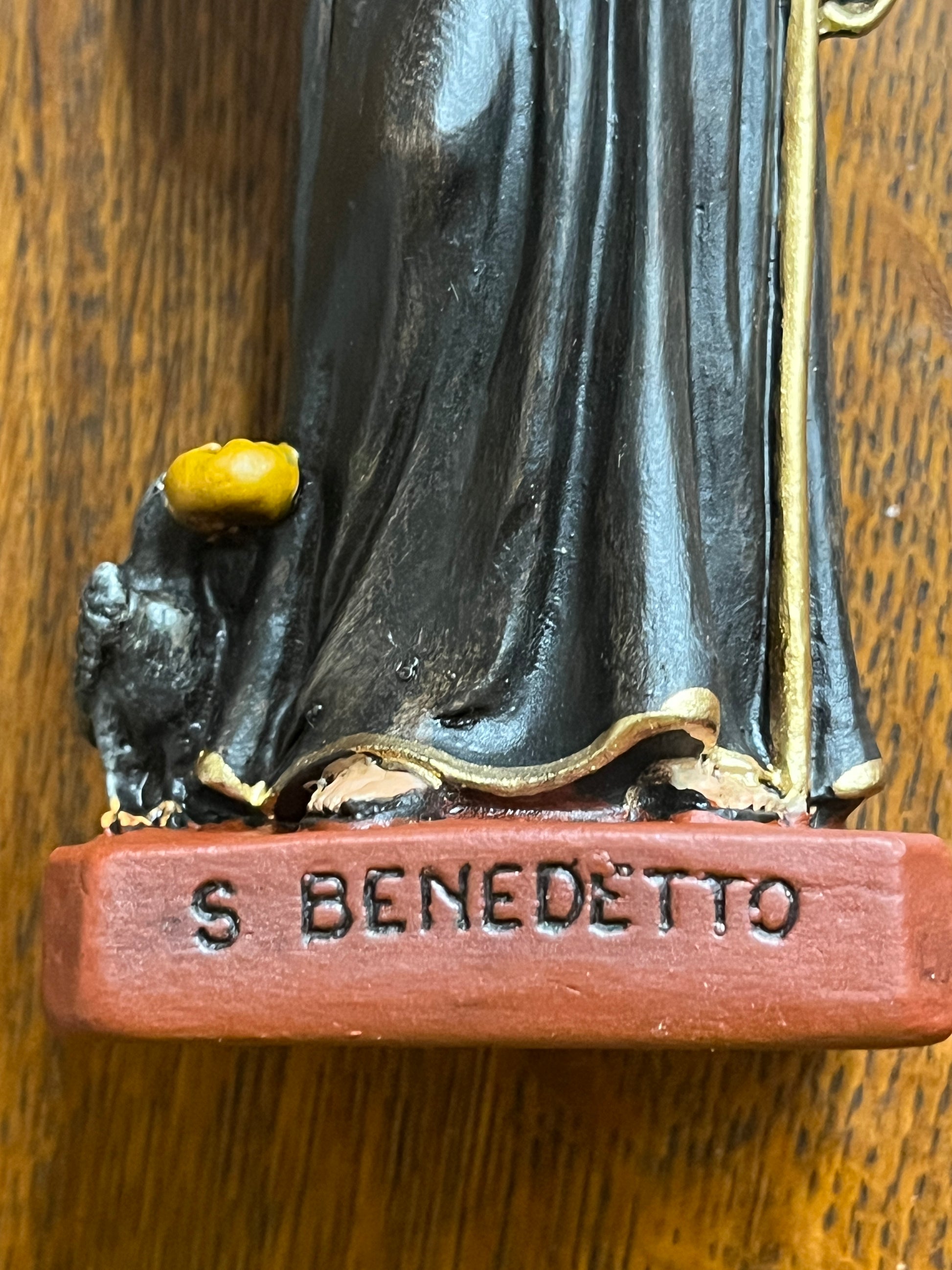 Close-up of 6 1/2" St. Benedict statue base with black robe, gold trim, and small raven holding a yellow object