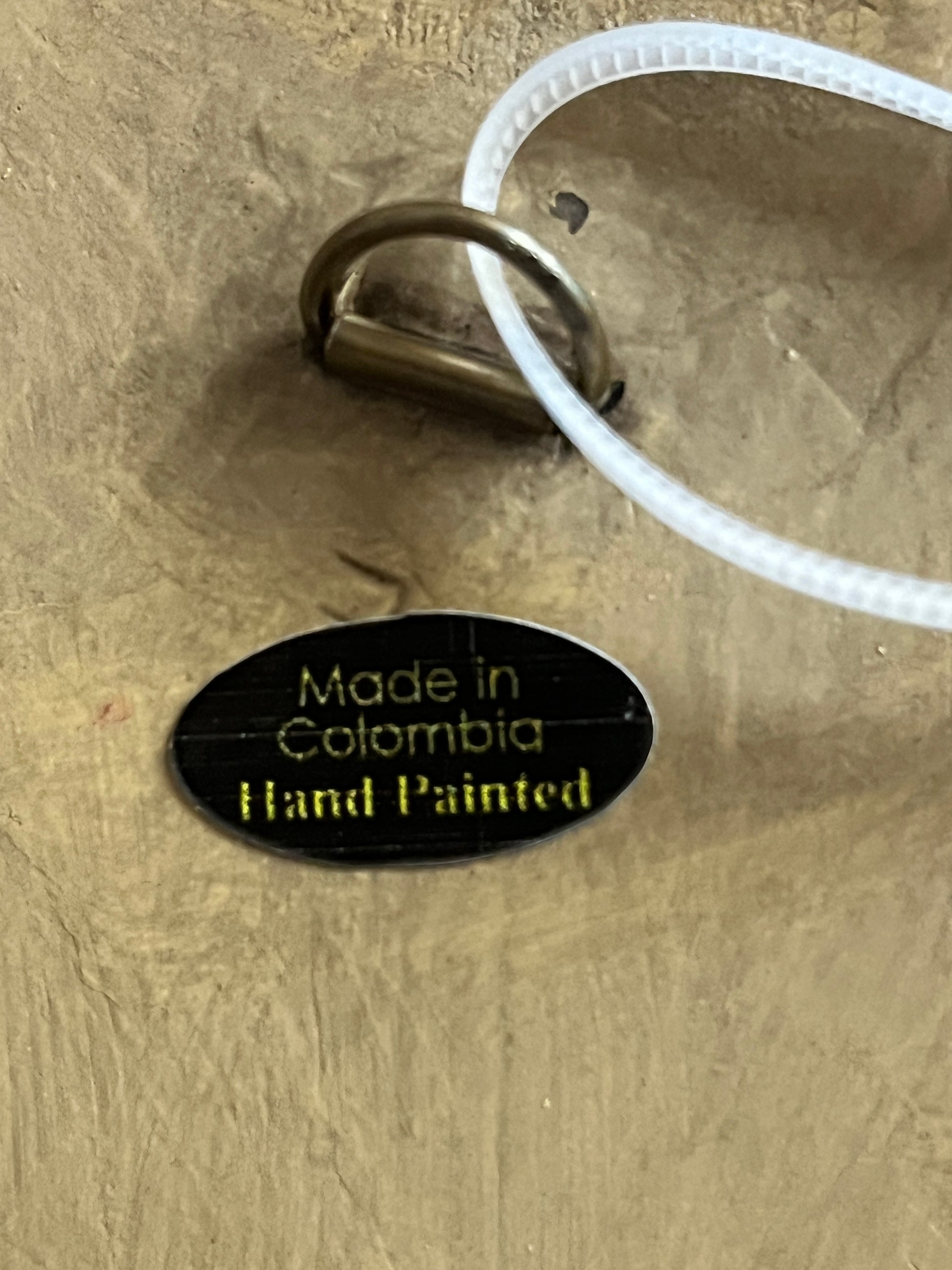 Oval black label with gold text reading Made in Colombia Hand Painted on wood plaque back