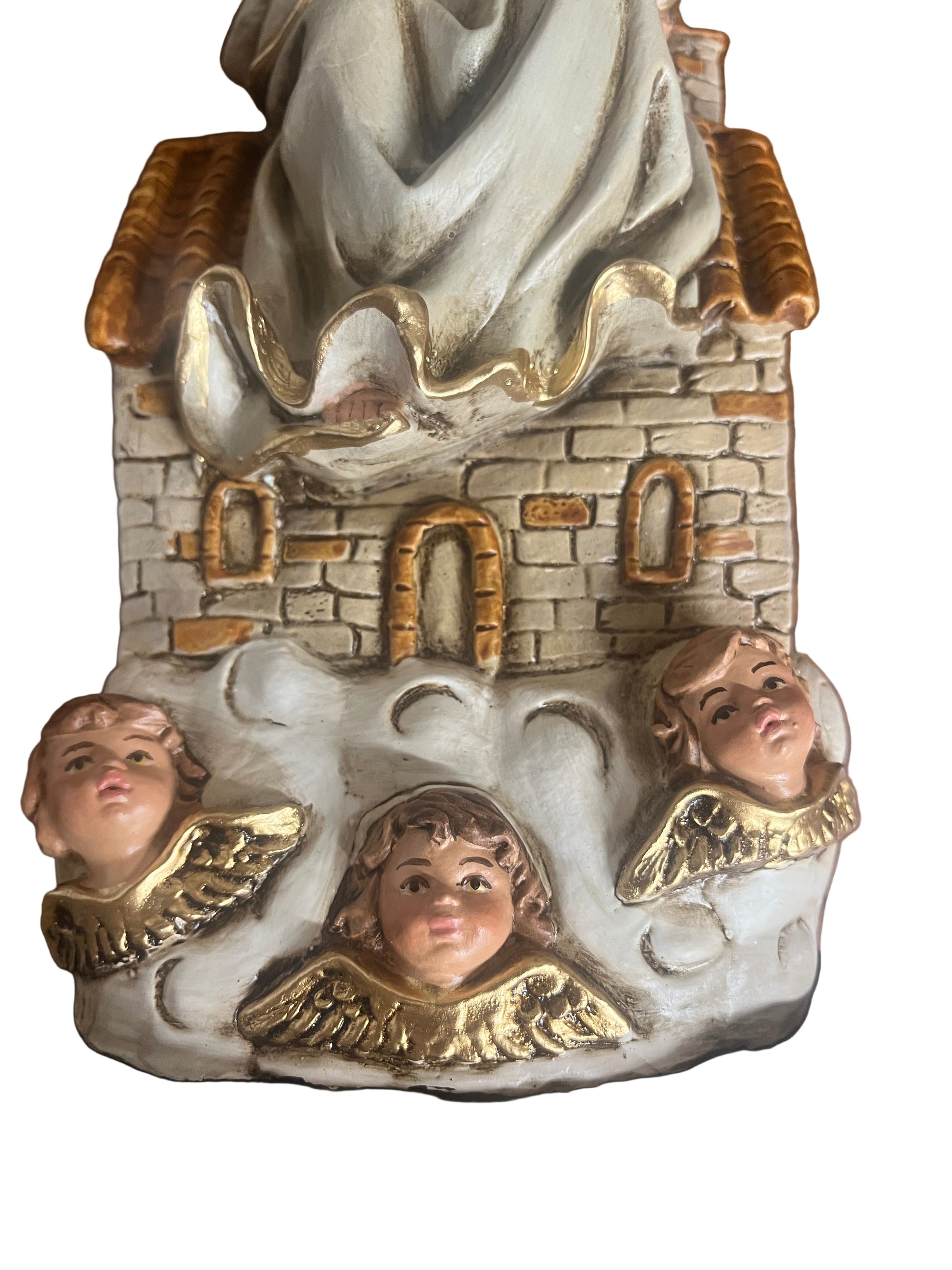 Base of Our Lady of Loretto statue showing stone house with three cherub heads and gold wing details