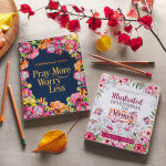 Pray More Worry Less guided coloring prayer journal with floral cover and matching floral gratitude journal on wooden surface